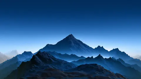 A sharp mountain peak rises above layered blue ridges under a clear evening sky.