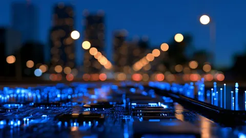 Blue-lit circuit board in the foreground, with a blurred city skyline and street lights behind it.