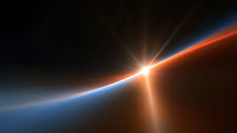 A bright star breaks over a thin curved horizon, with copper light on one side and deep blue on the other.