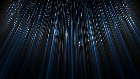 Fine streaks of blue light pour down from above, spreading out like a veil over the dark.